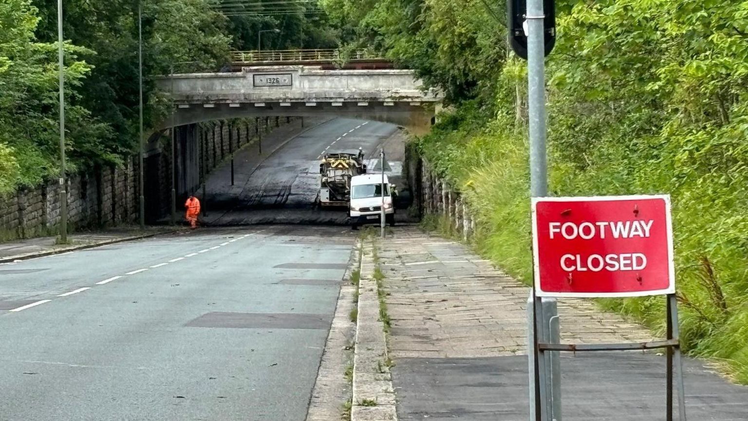 A person in a hi-vis jacket walks out from under the railway bridge 