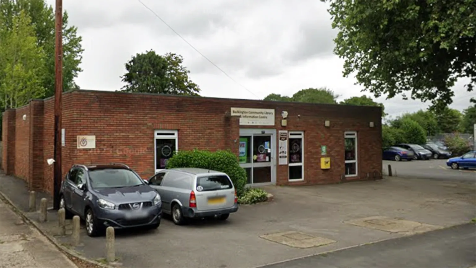Google Bulkington library is a brick building. Above the door a sign reads: "Bulkington Community Library and Information Centre". In the front of the building are two cars