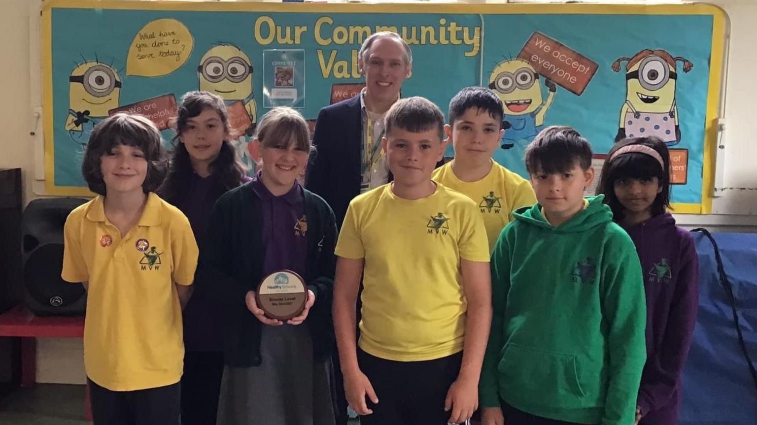 Pupils and staff member in school hall with bronze plaque