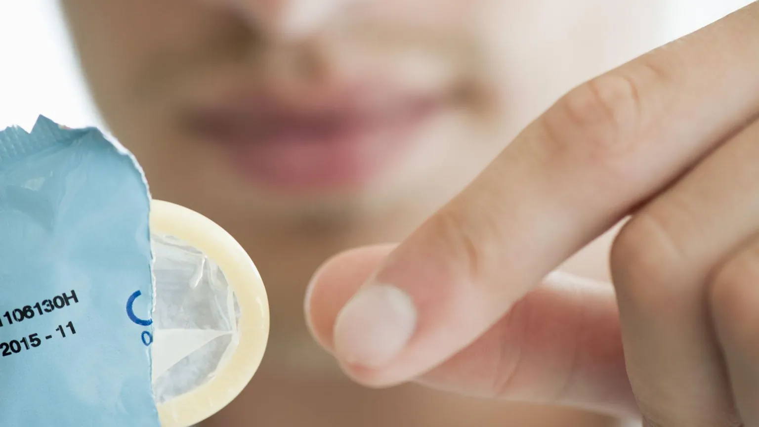 Getty Images A man holds an open condom packet. He is about to remove the condom, which is poking out.