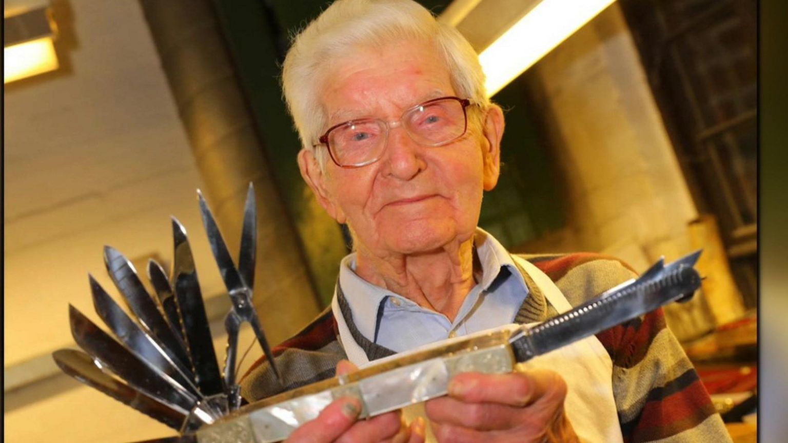 An elderly man with glasses holds a huge pen knife 