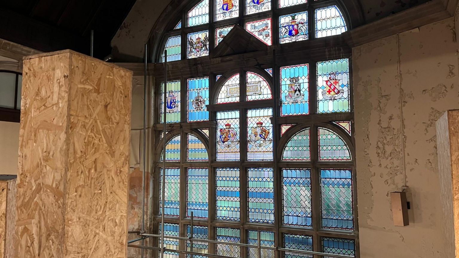 A stained glass window with scaffolding and a wooden plinth in front of it