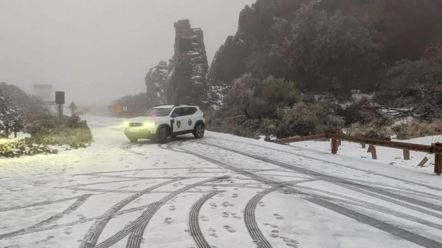 An emergency services car parked across a snow-covered rural road in fog