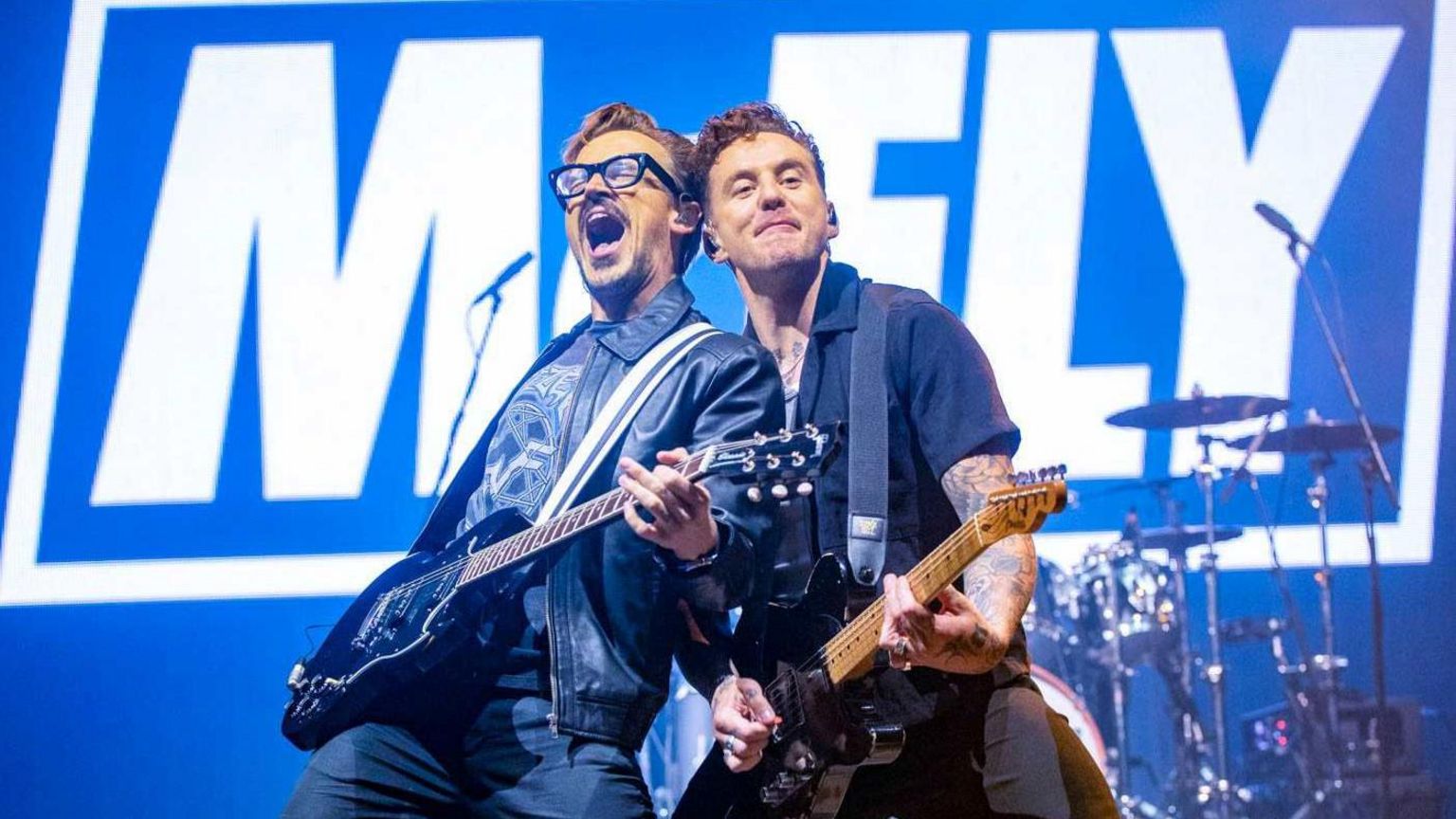 Two members of McFly on stage holding guitars