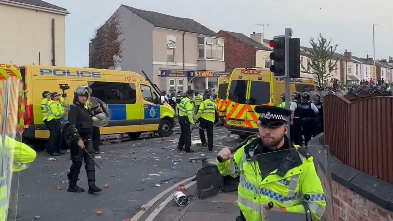 Yellow riot police vans and officers in riot gear and high-vis yellow jackets, on a street in Southport during the unrest