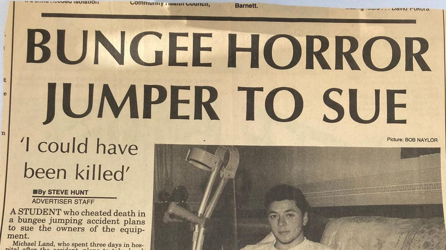 A picture of a newspaper clipping showing Mike shortly after the accident. The headline reads "bungee horror jumper to sue", and includes a large picture of Mike sat on a sofa with a serious expression, holding a pair of crutches. 