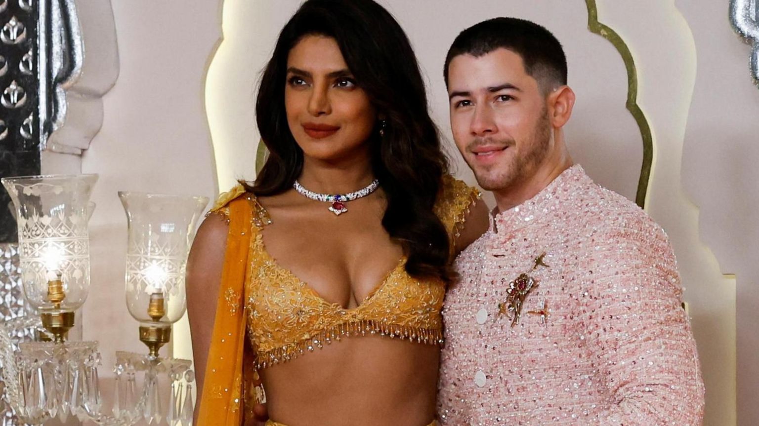 Priyanka Chopra and her husband Nick Jonas are both dressed in lavish wedding outfits, smiling at the cameras.