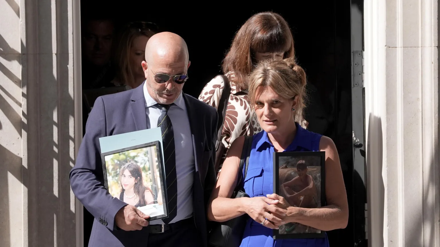 PA Media A man in a dark suit and a woman in a blue dress exit 10 Downing Street. They are carrying framed photos of their children.