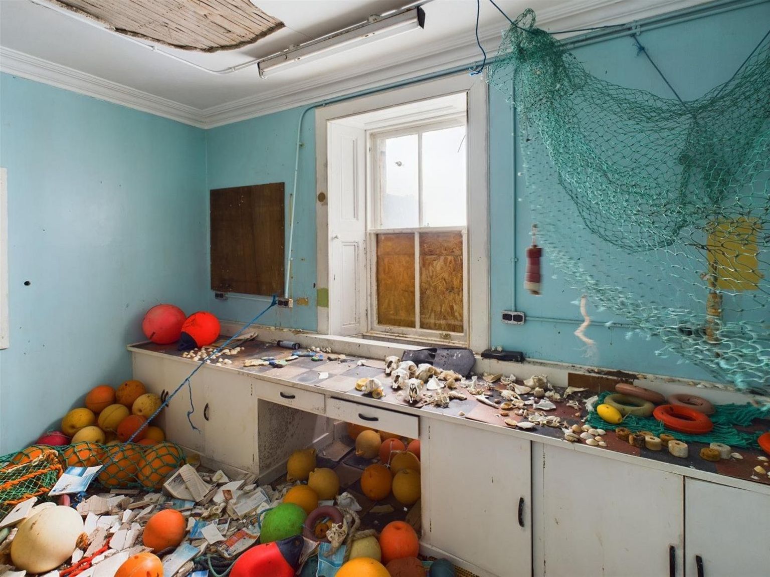 Interior of a bright blue painted kitchen with life buoys scattered on the floor and countertops and fishing net hanging on the wall