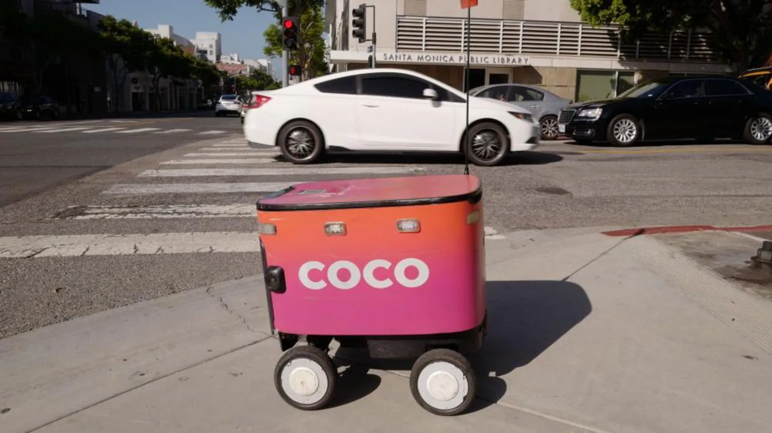 Coco A delivery robot in front of a car on a street in Los Angeles