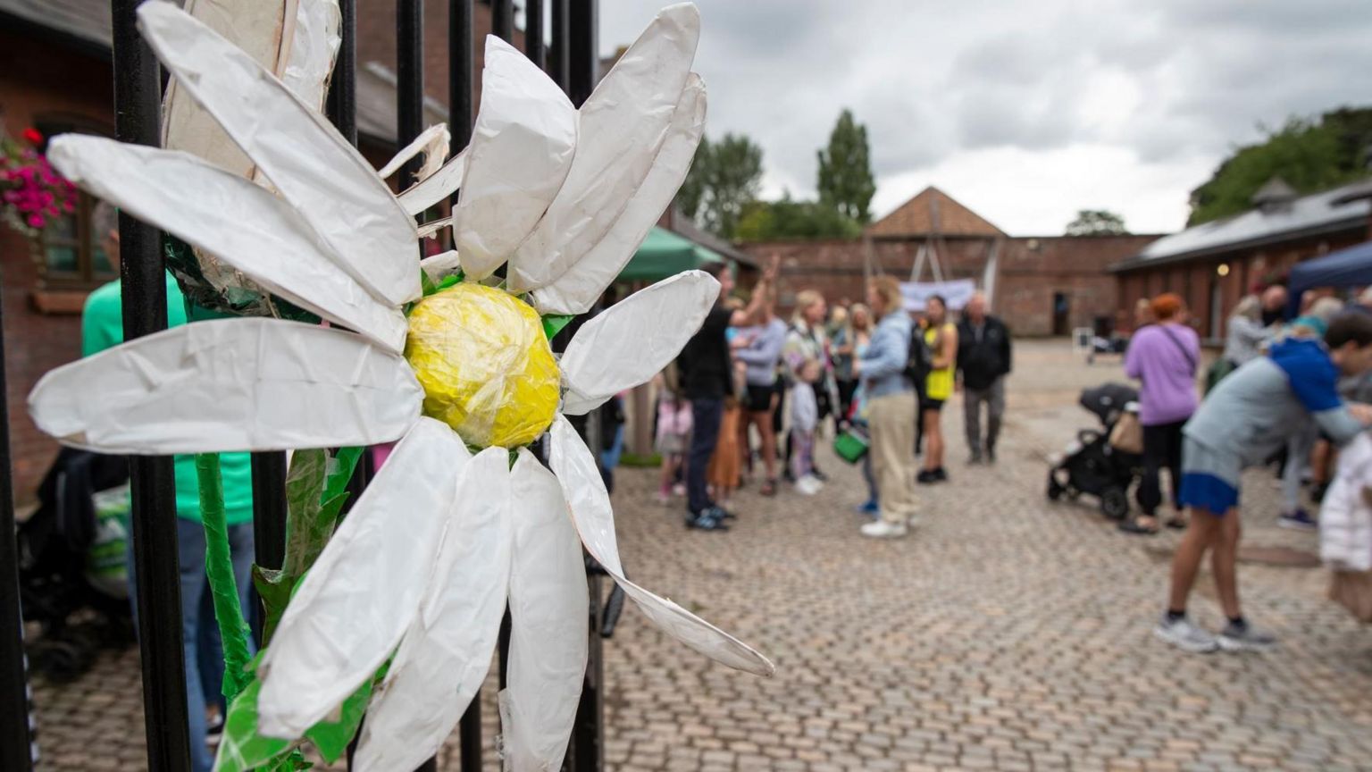 Flower art attached to gate of court yard with people at stalls