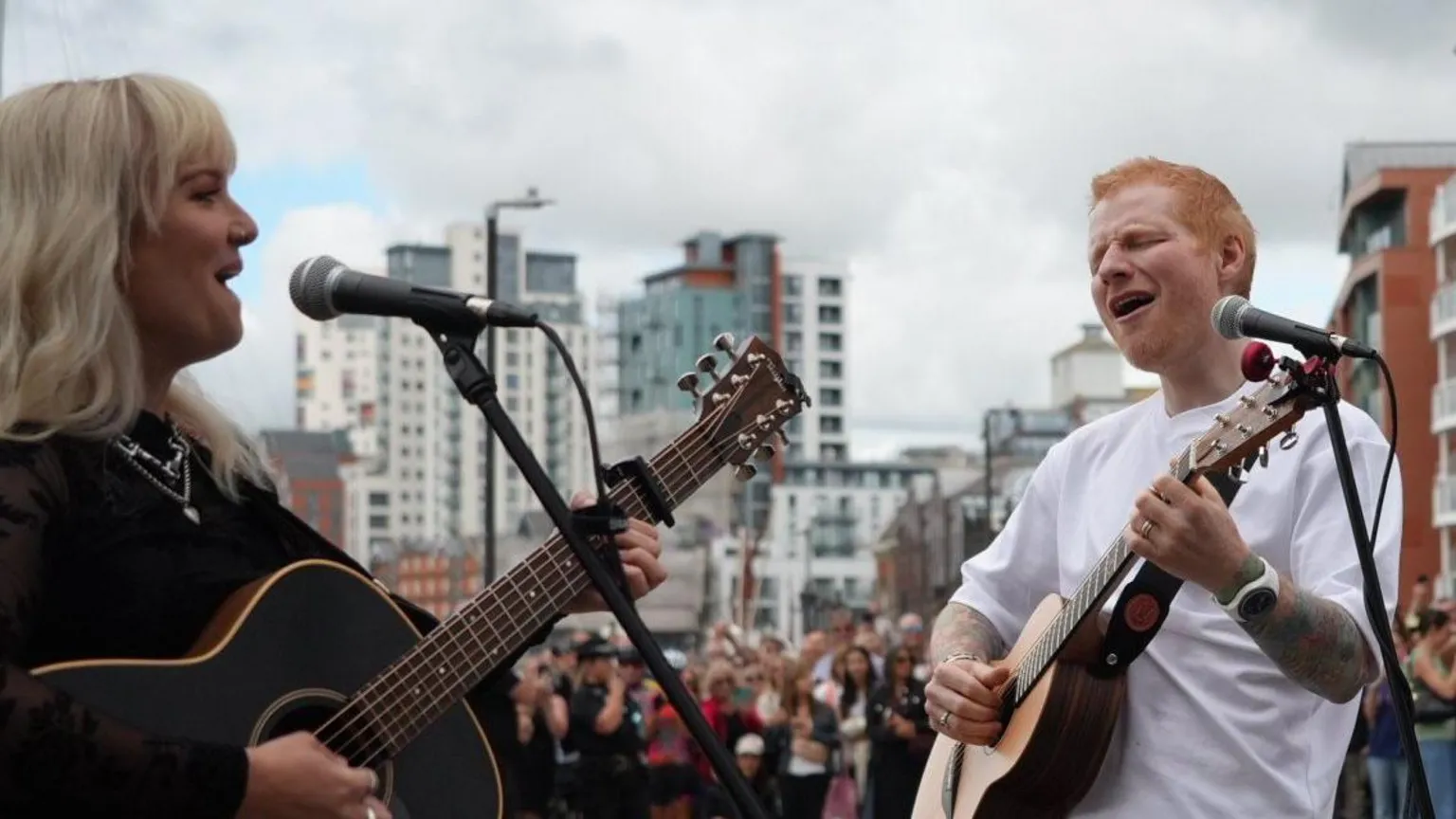 Shaun Whitmore/BBC A man with red hair and a white T-shirt plays a guitar alongside a woman with blonde hair and a black top.