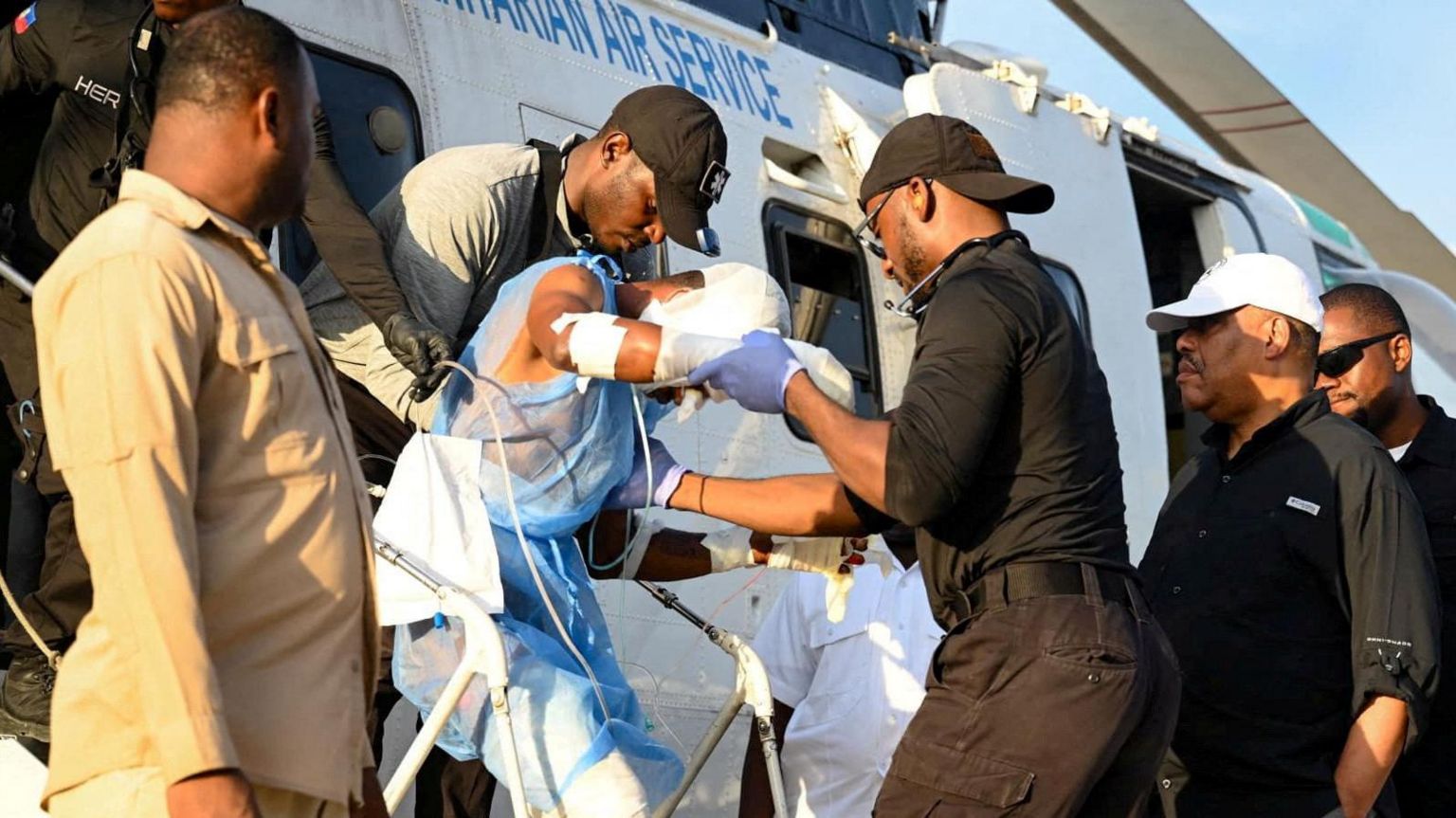 A man wrapped in bandages is helped off a helicopter by a group of men