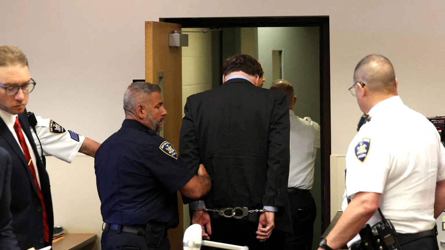 James Carbone/Pool via REUTERS Gilgo Serial Killer Rex Heuermann is seen from the back with his hands cuffed behind him as he is escorted by several uniformed police through a doorway le4aving the courtroom.