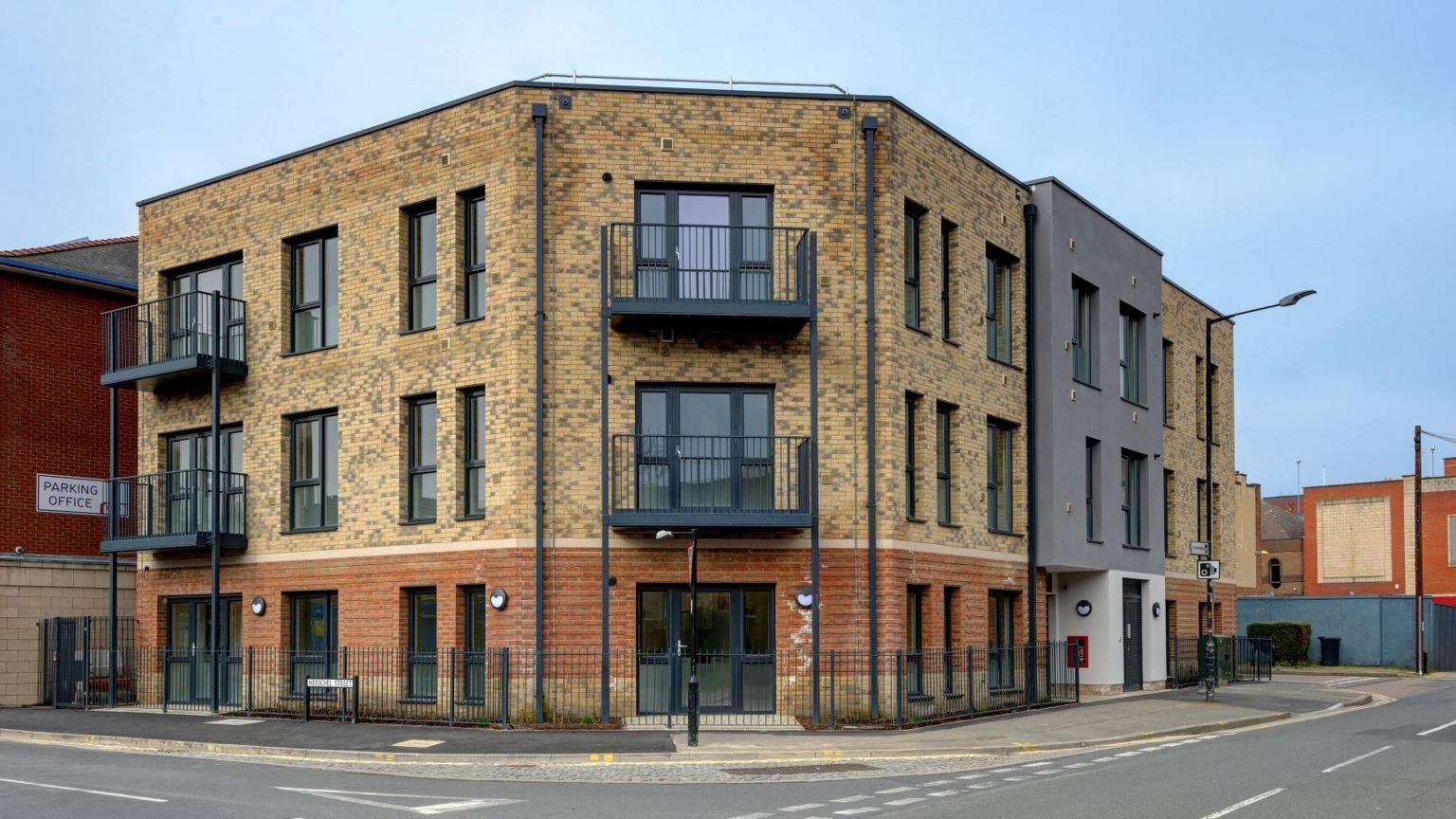 A three-story block of flats with a modern-looking brick exterior with black window frames and balconies.