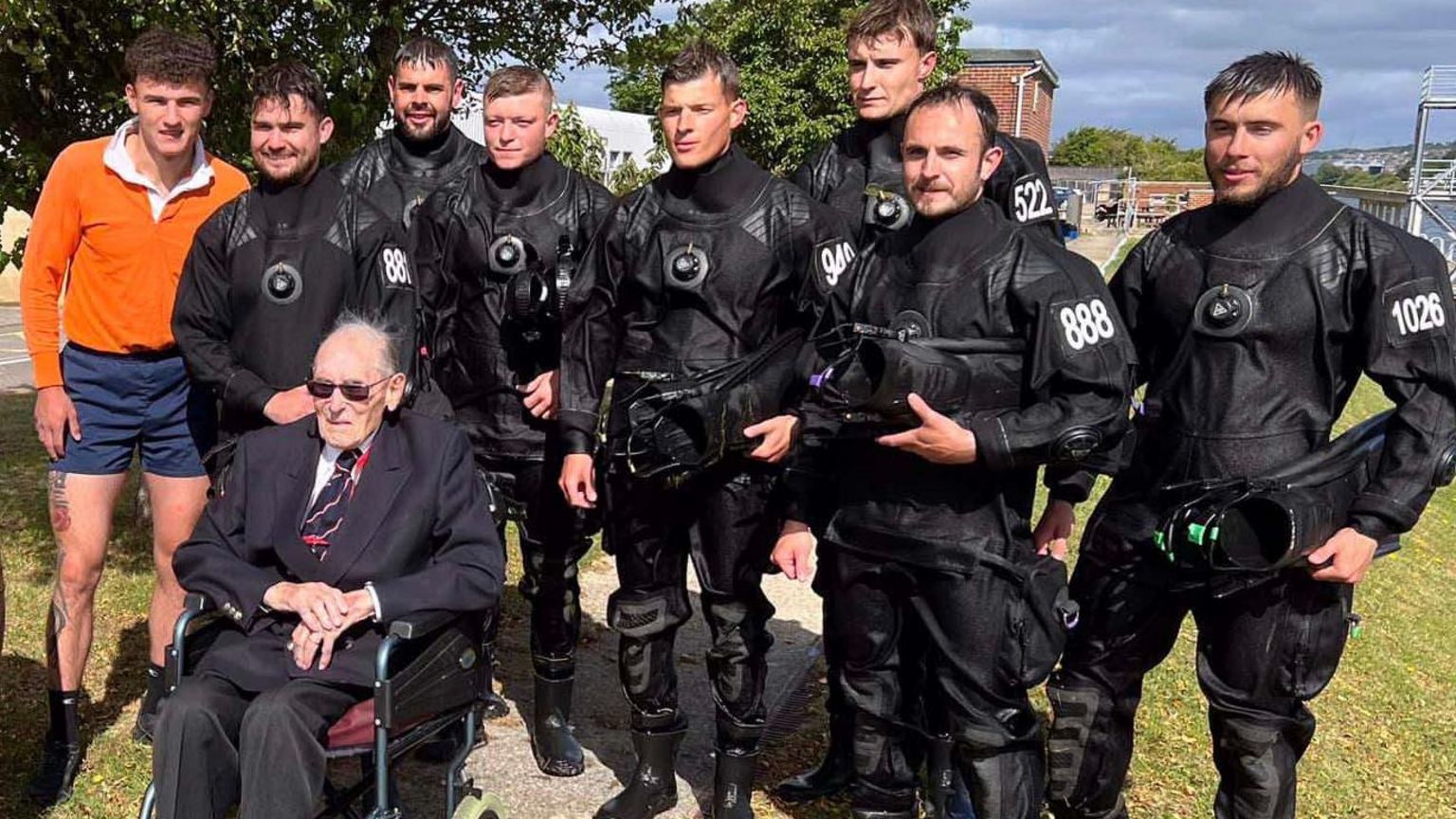 War veteran Boyd Salmon sits in a wheelchair at the Royal Navy's Portsmouth base surrounded by eight members of the navy's current diving team