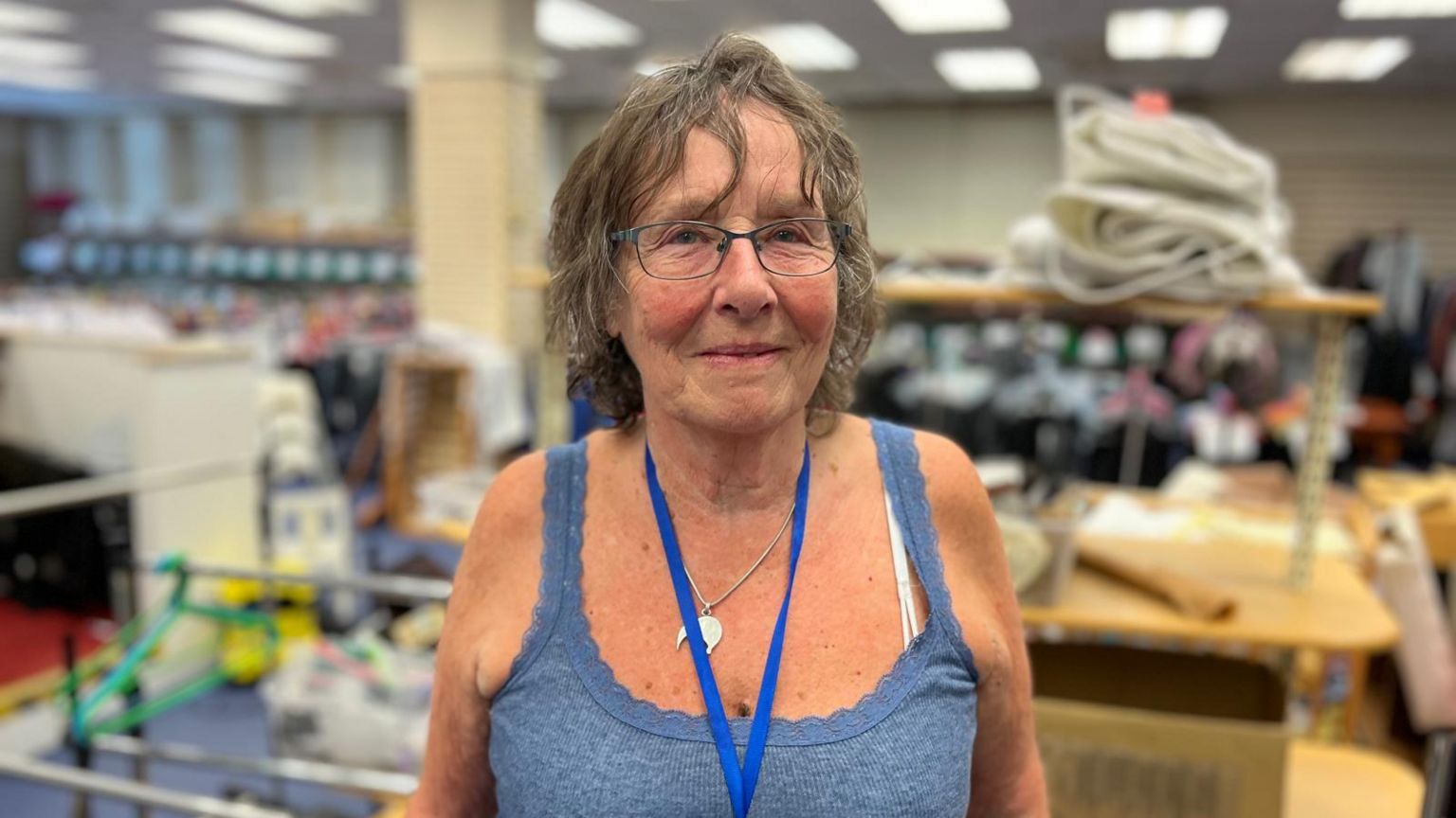Jane Robinson looks into the camera, wearing glasses, standing in a shop unit