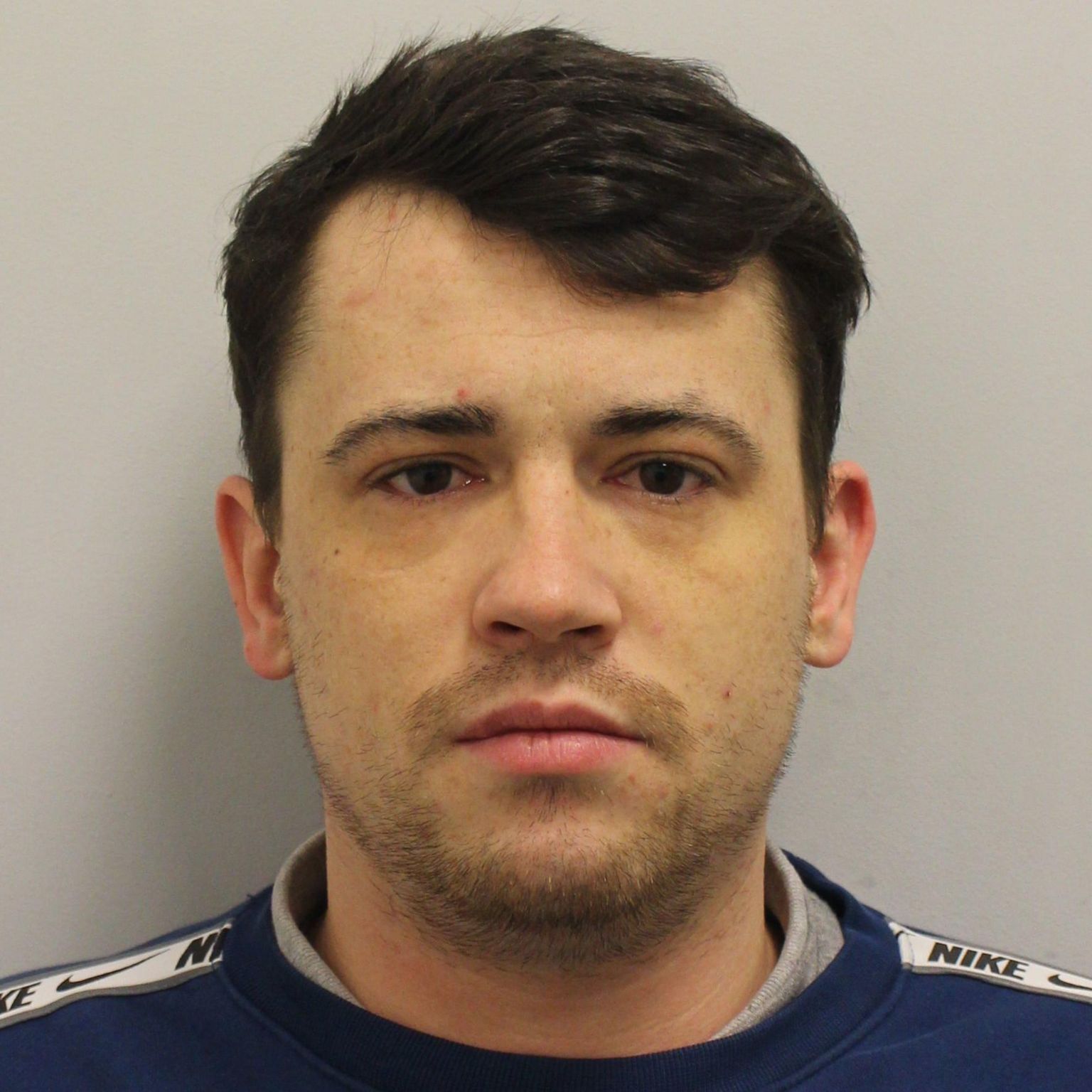 Custody image of Jordan McSweeney, a  young man with dark hair wearing a dark blue sweatshirt and grey tshirt