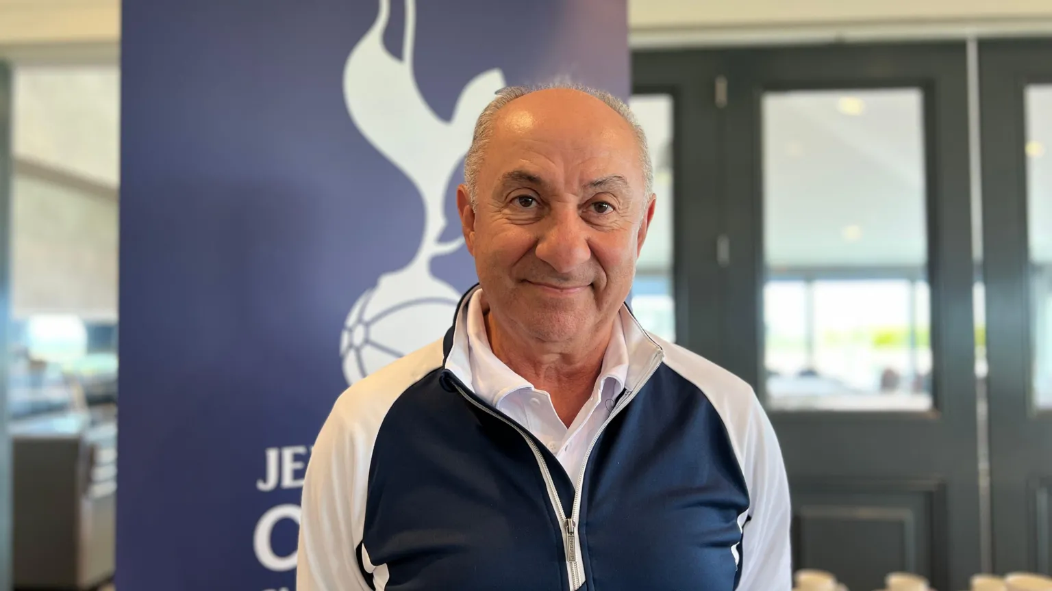 Ossie smiles at the camera with a Jersey Spurs Supports banner pulled up behind him in the golf club