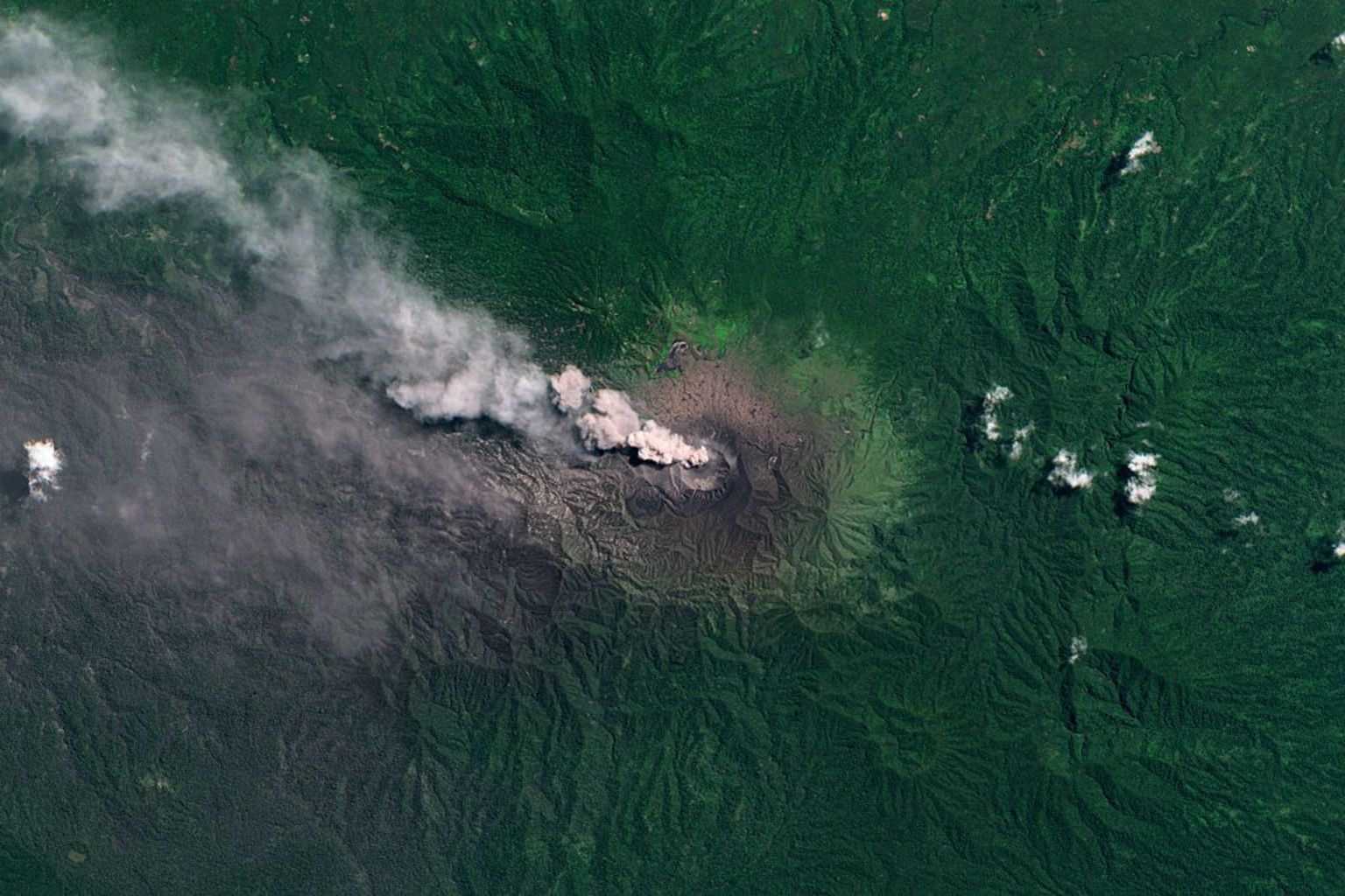 杜科诺火山的卫星影像,可见火山口喷出烟柱,周围被茂密的绿色植被环绕