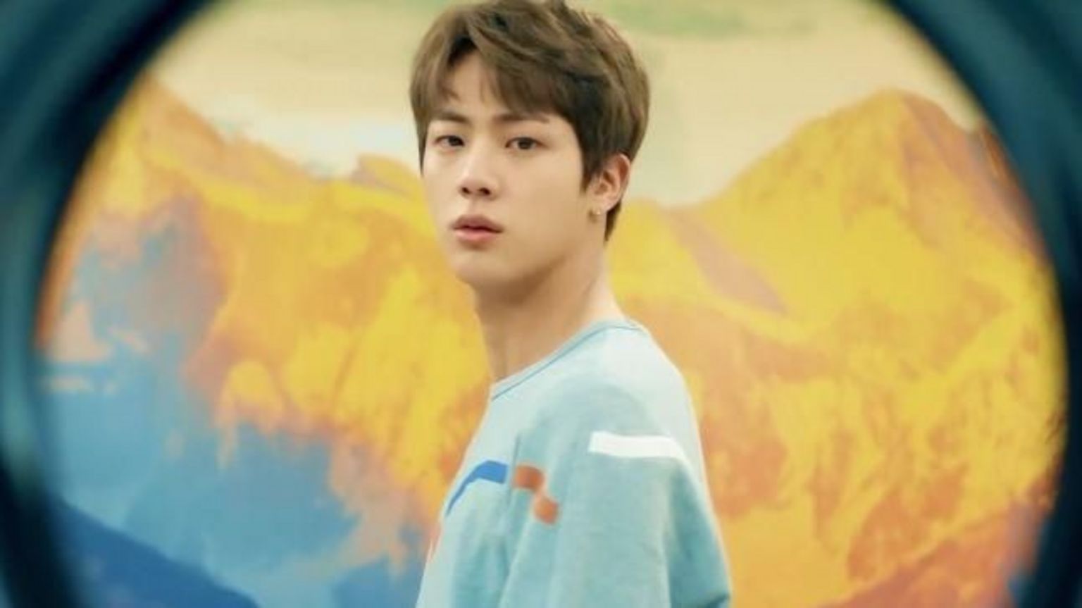 韩国流行音乐(K-pop)组合防弹少年团(BTS)的一名成员直视镜头,身后是泛黄的山脉。