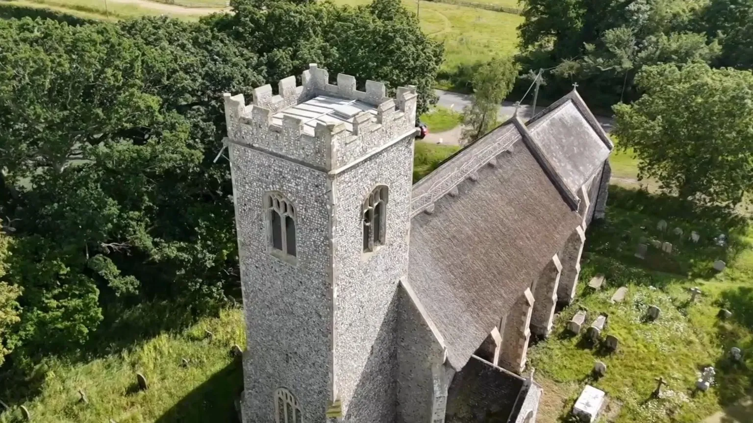 A church pictured from above, with a graveyard around and headstones. There are trees.