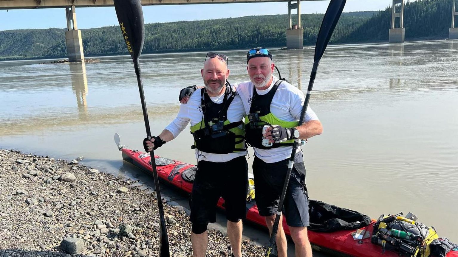 Chris Davidson and Nick Hobley standing by their kayak alongside the river