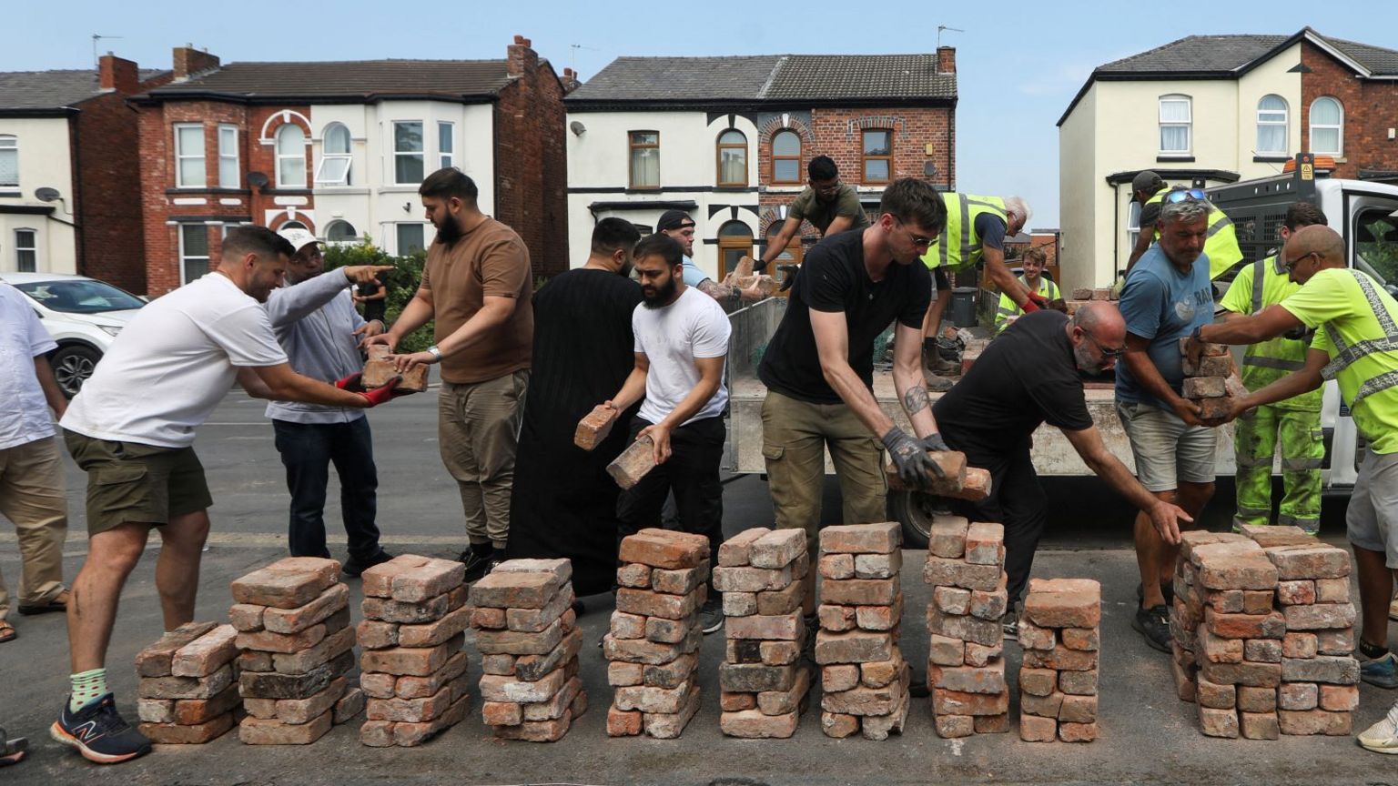 A group of men stand in front of piles of bricks as they prepare to rebuild a wall in Southport