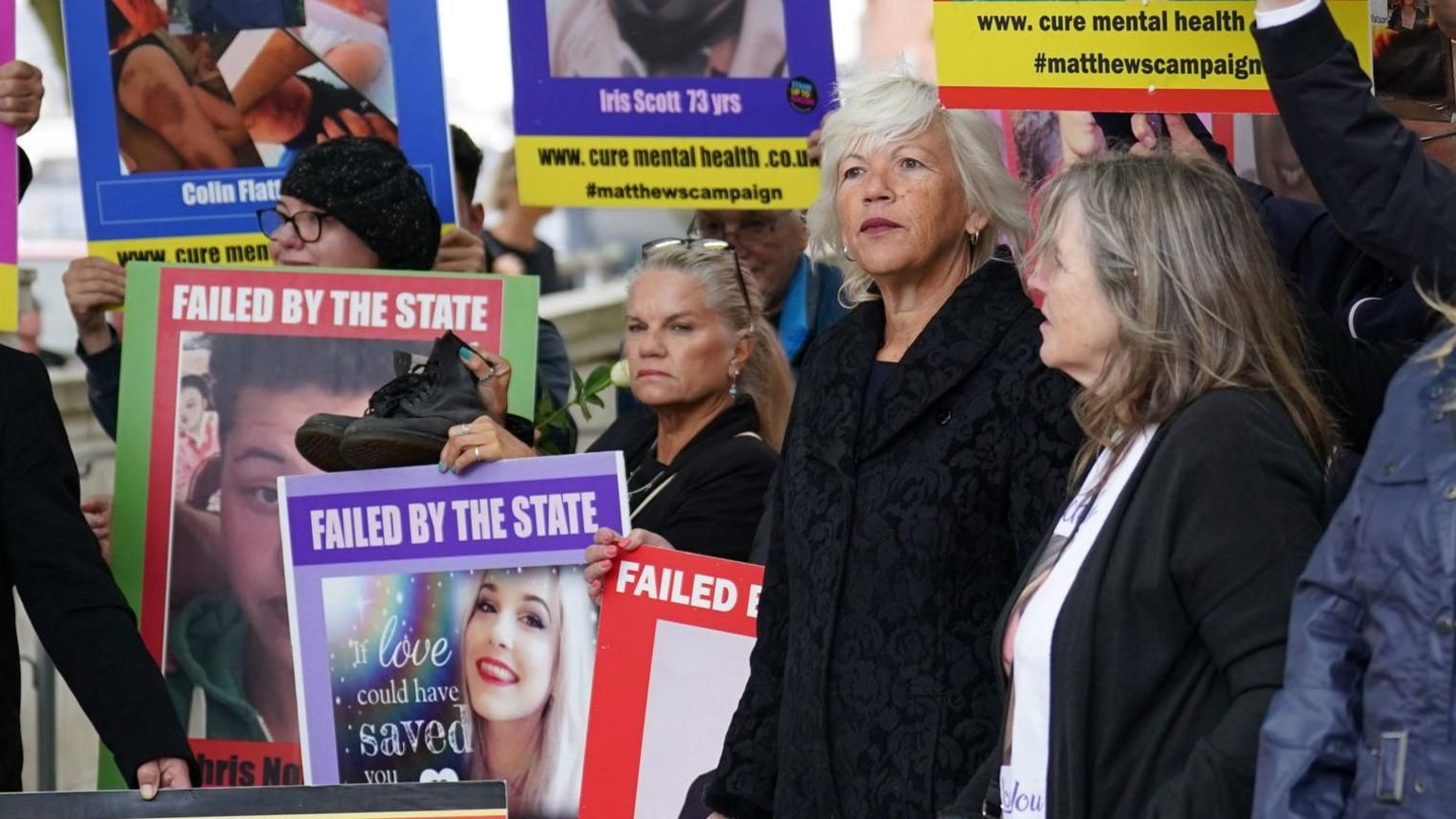 Family members holding placards featuring pictures of their dead relatives while standing outside the Lampard Inquiry in Chelmsford