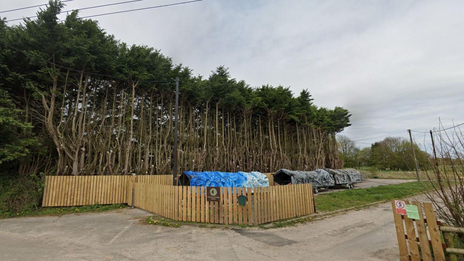 The entrance to Thoulstone Park, with a wooden fence and trees