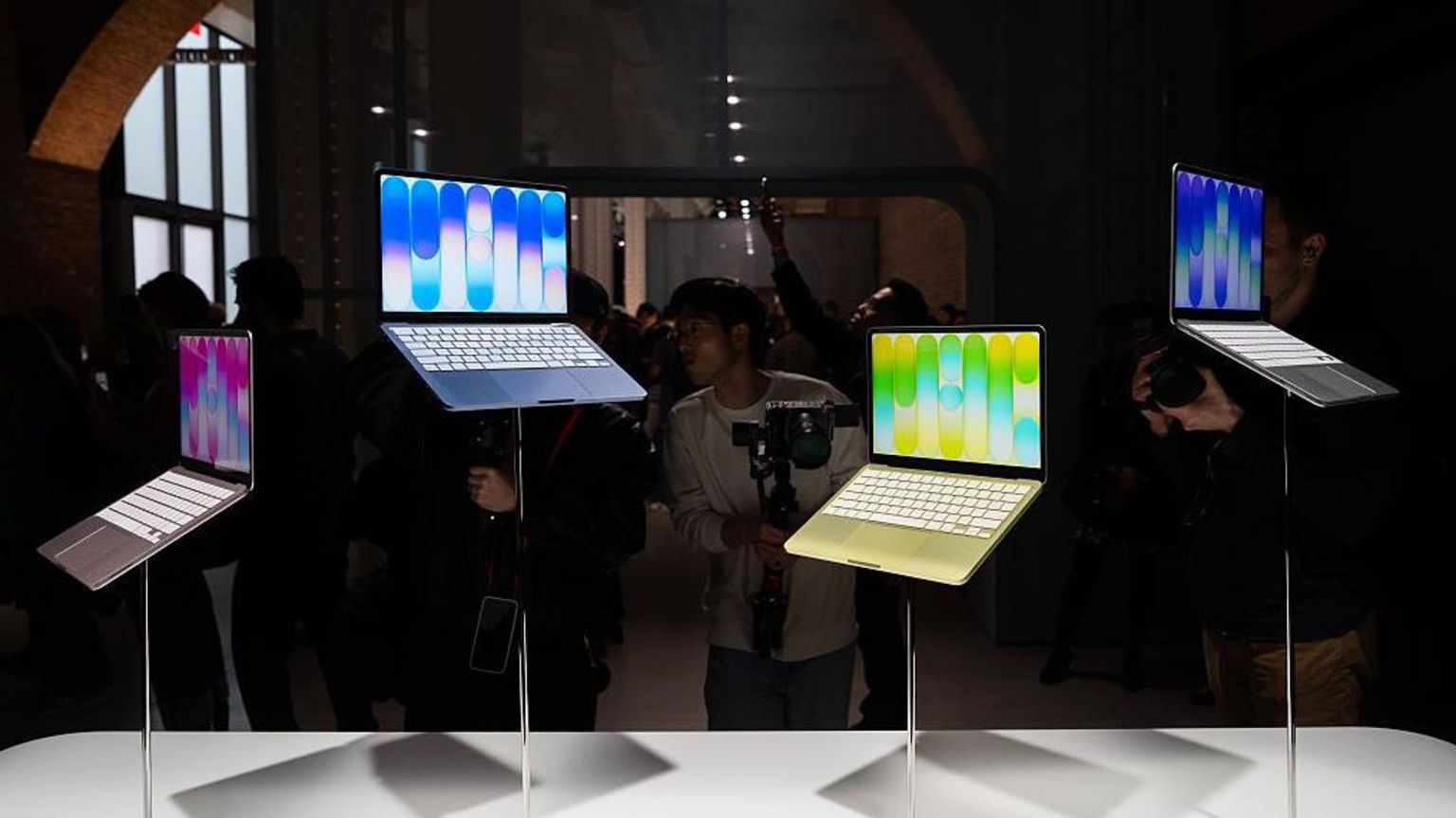 在苹果专门店的展示区内,多部色彩鲜明的 Apple Neo 笔记型电脑以不同高度陈列于展示架上,周围挤满摄影师争相拍摄。