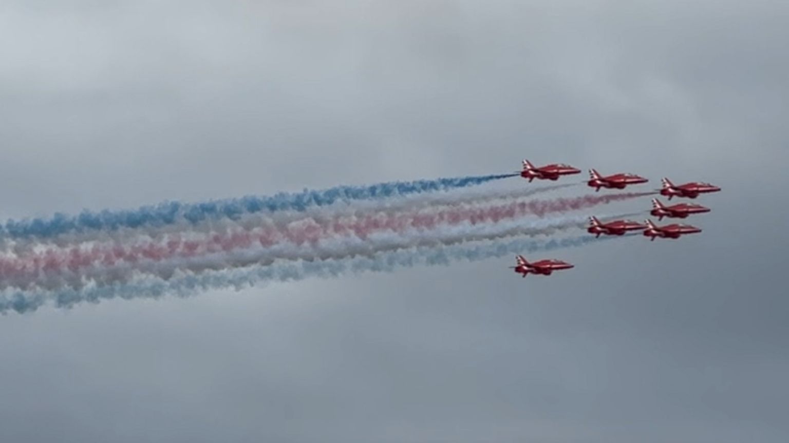 The Red Arrows in formation with blue and red smoke coming from their tails