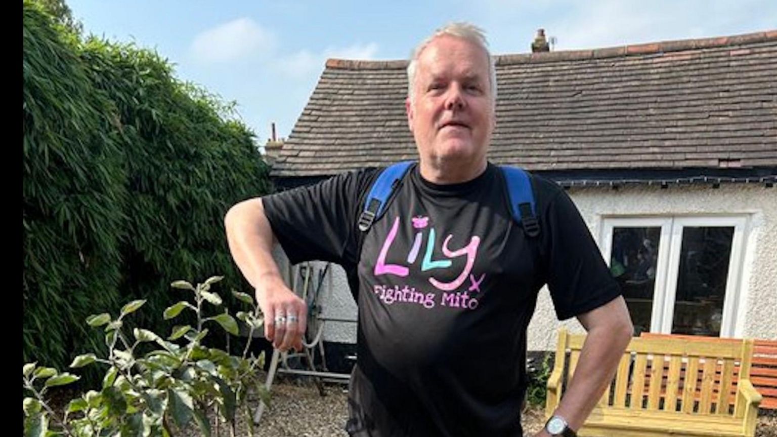 Kevin Day with a lily foundation t shirt on. He stands in a garden