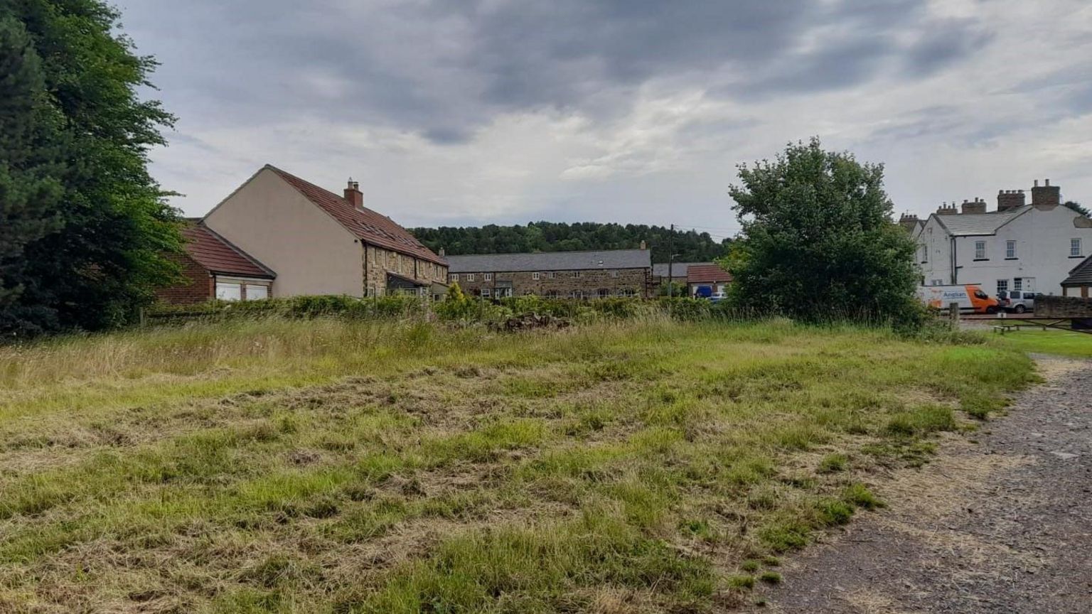 Houses in a rural area near grassland and a poorly paved path.