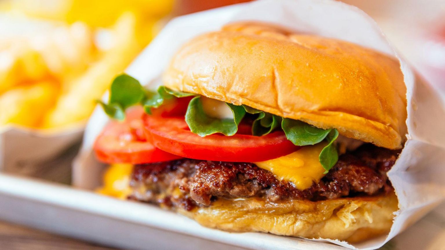 Close-up shot of cheeseburger with lettuce and tomatoes and fries in background