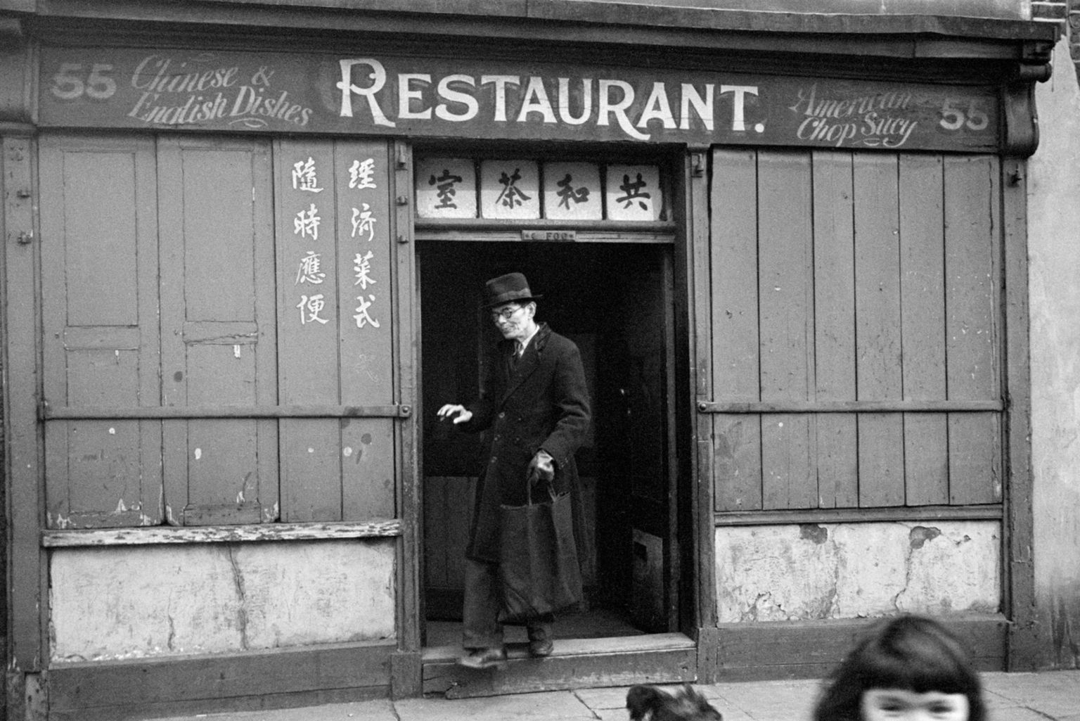Black and white photo of a man in a black coat leaving a Chinese restaurant in Limehouse in 1946