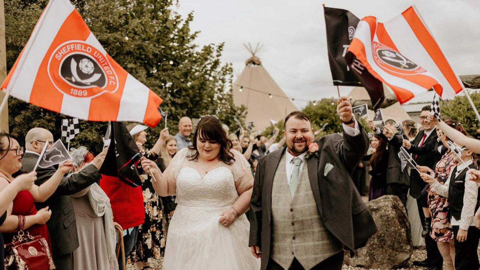 A couple had confetti thrown over them by wedding-goers with flags waving behind them