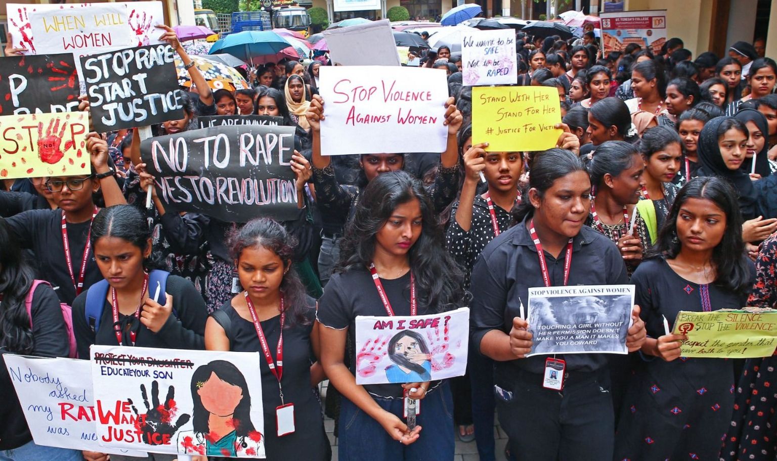 A large group of women wearing black tops holds up placards during a protest on violence against women