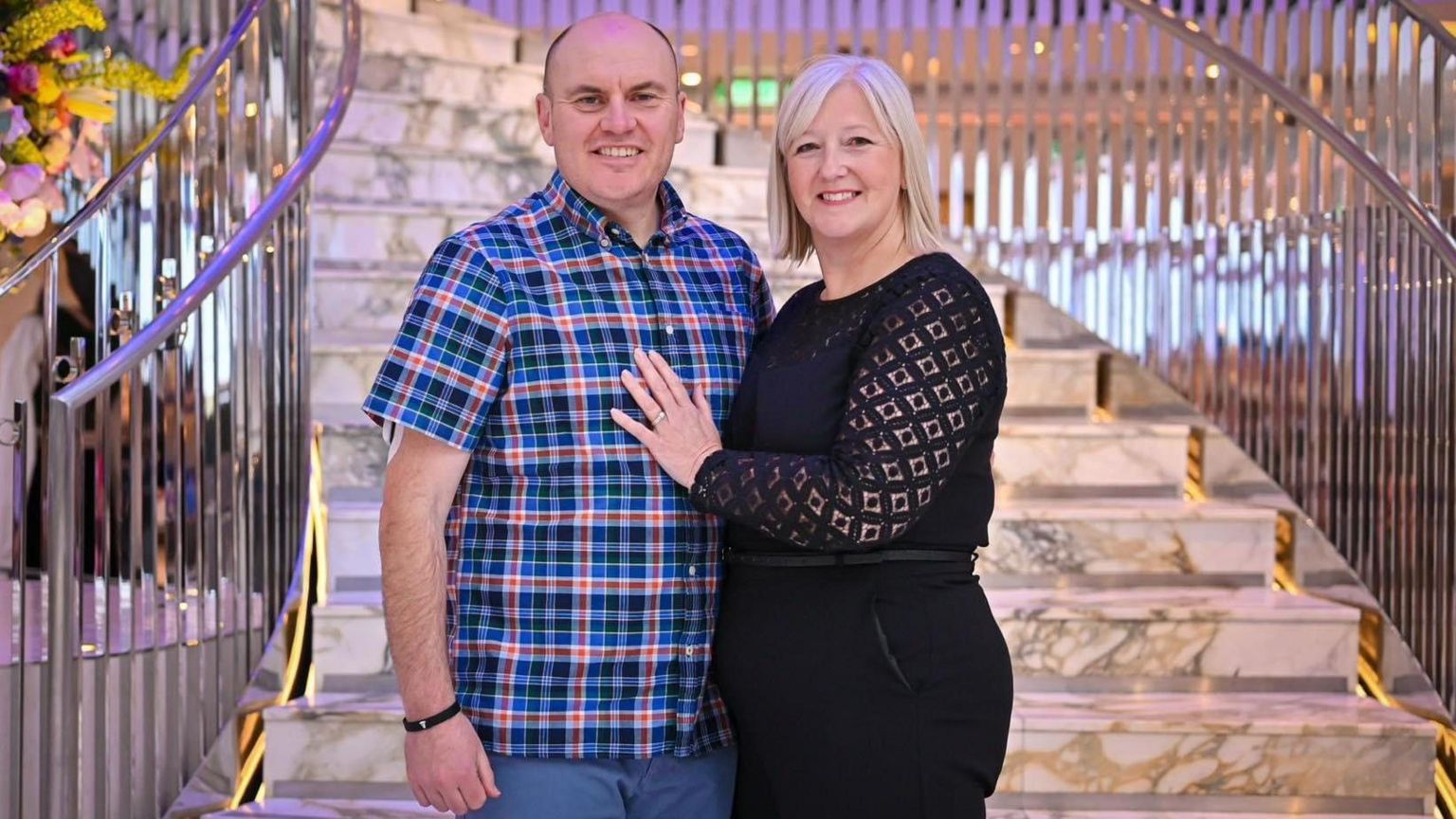 Man in checked shirt with woman in black outfit smiling and standing on steps