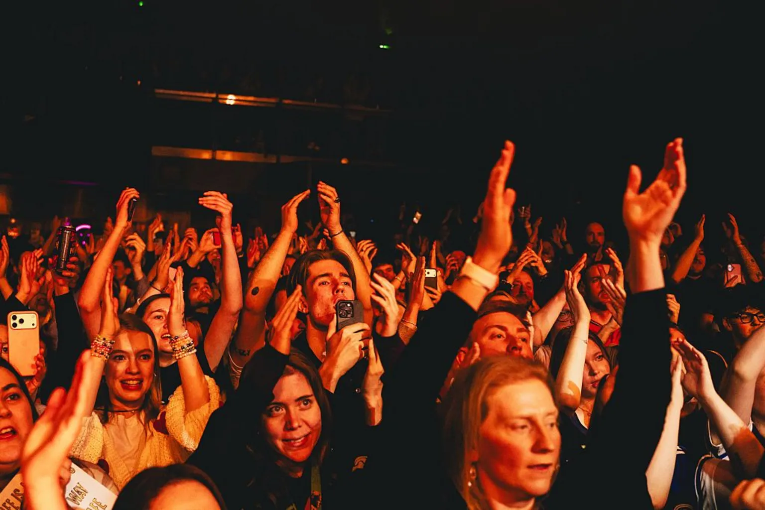 Getty Images A view of the crowd during a Myles Smith show - the crowd's hands are in the air and people are smiling, while illuminated dark orange from the stage lights.