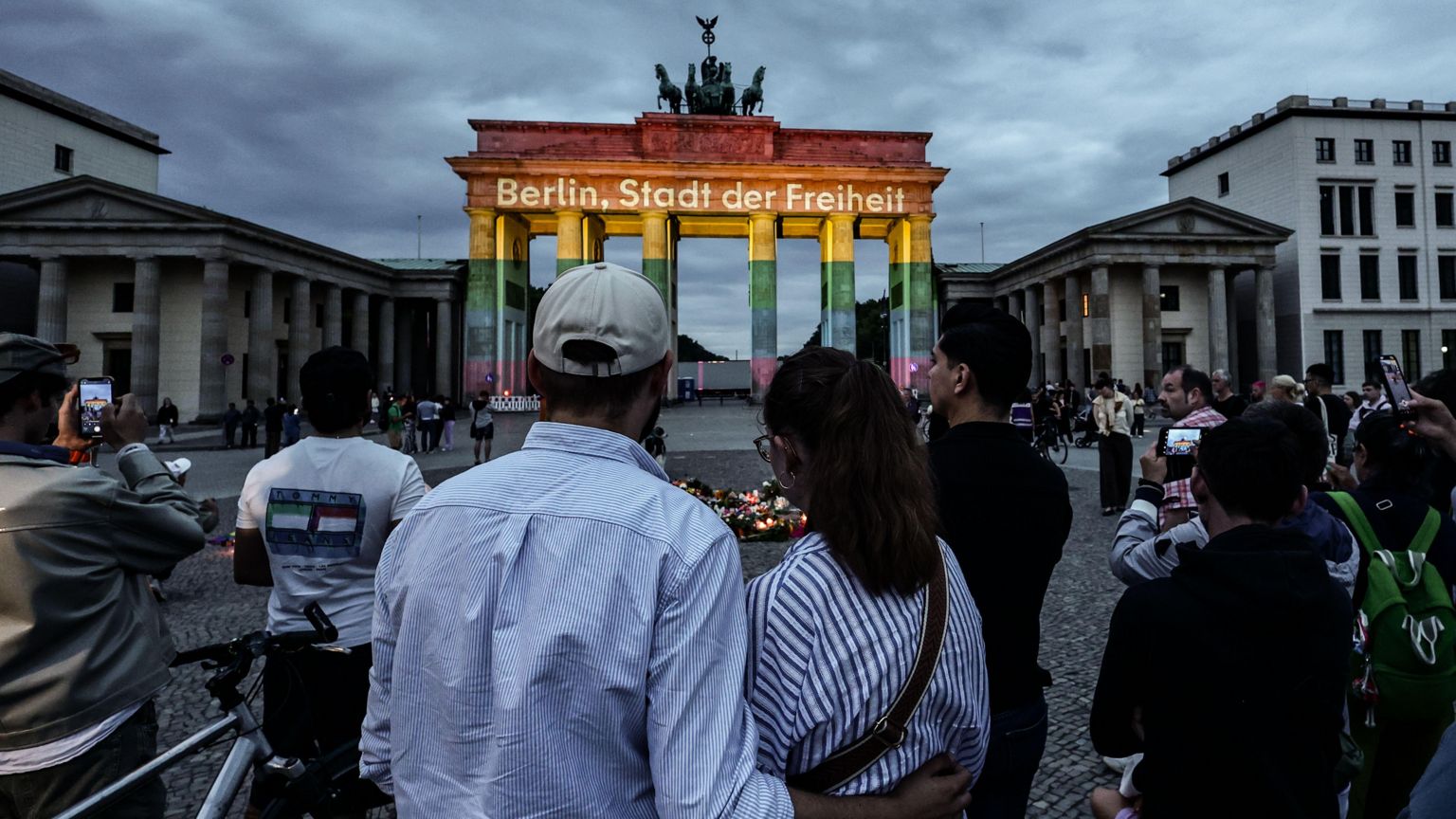 人们在勃兰登堡门前悼念,勃兰登堡门亮起“Berlin, city of freedom”讯息灯光。德国柏林2026年7月26日,在克里斯托弗街日(CSD)巡游路线旁一辆汽车冲入人群的事发地点附近。