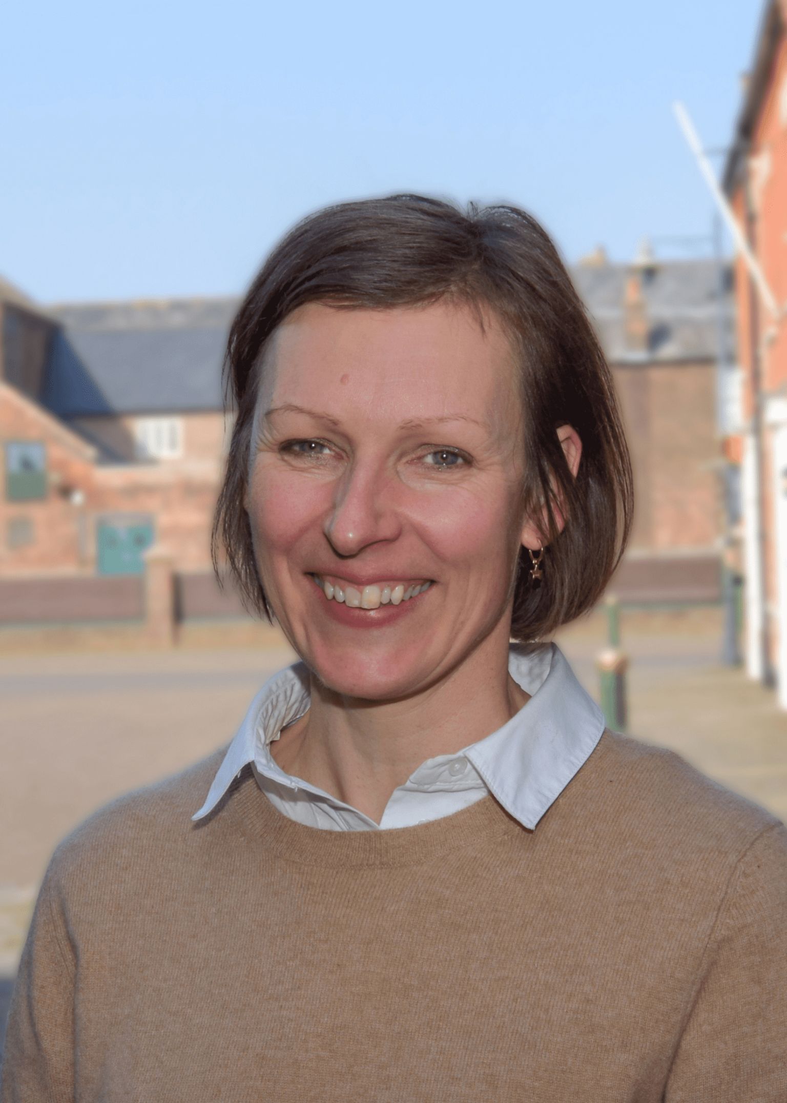 Vicky Etheridge a white woman with medium brown bobbed, thin hair at the ear, wearing a white shift covered by a camel wool sweater