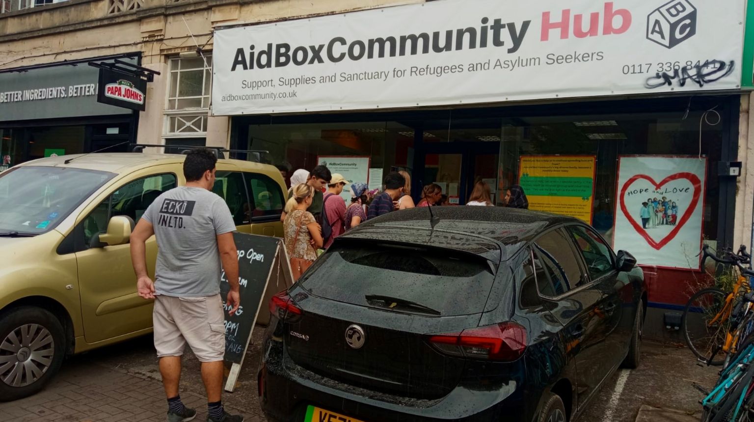 A picture of people queueing out the door of the current Aid Box Community Hub building. 