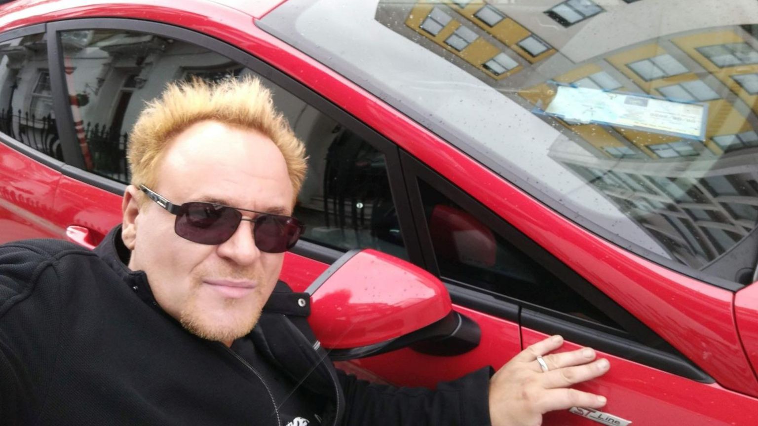 Mik Scarlet next to his car with blue badge on display