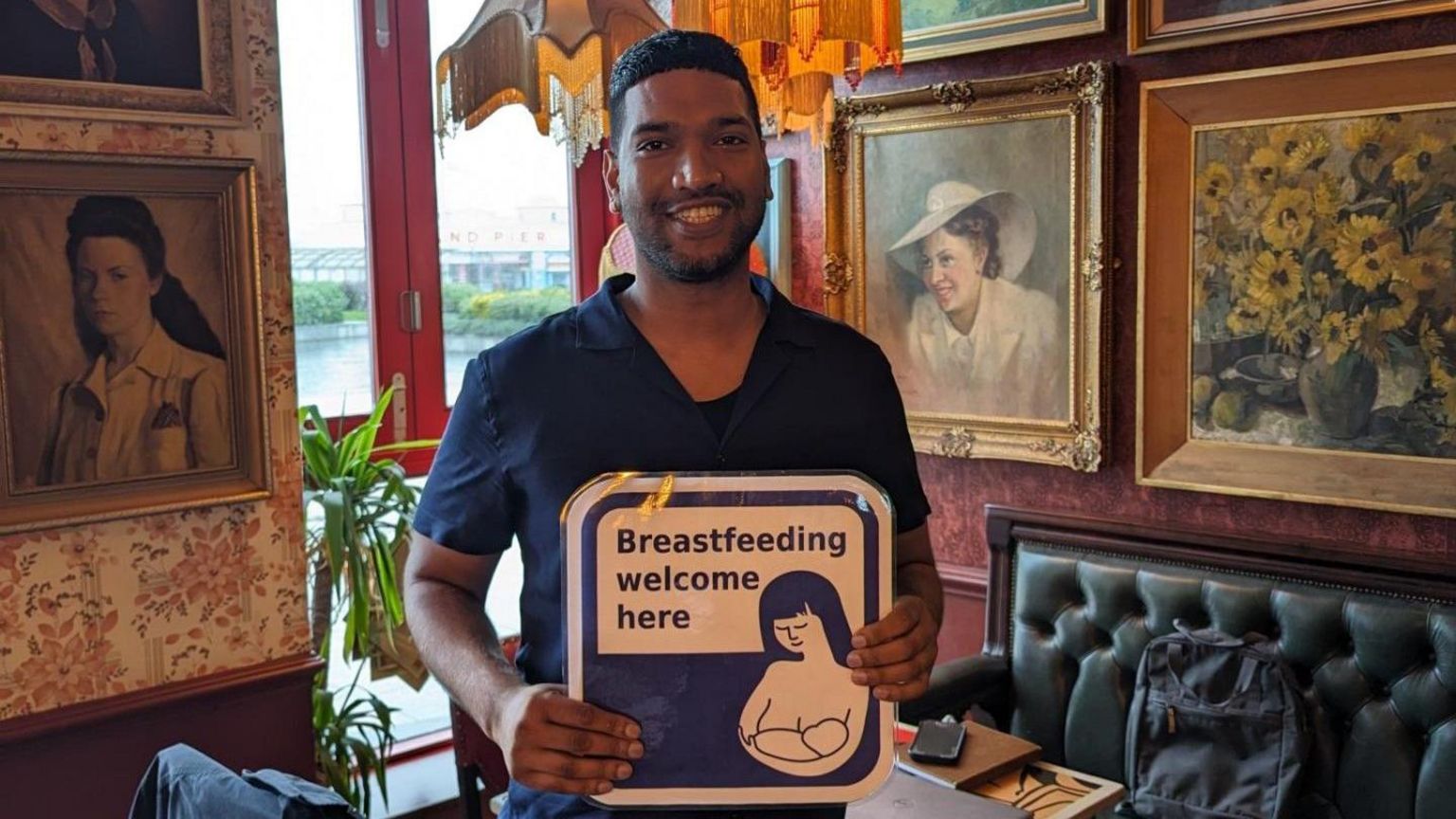 A man holding a sign which says 'breastfeeding welcome here'