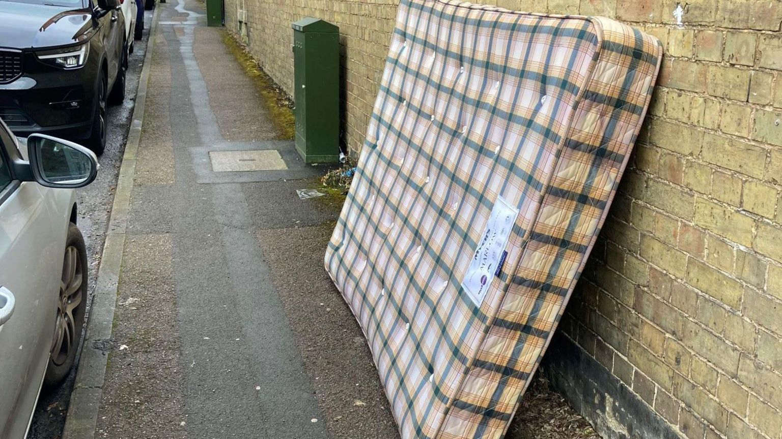 A mattress on a pavement and leaning against a wall 