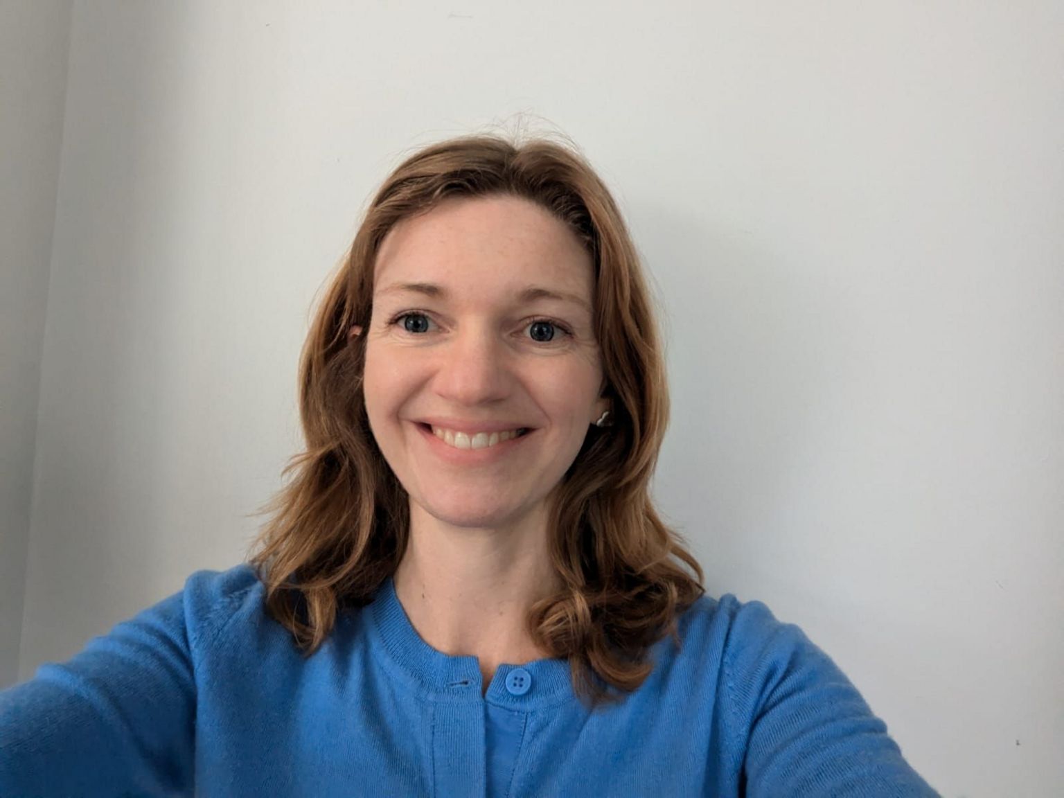 A smiling Anna Kenyon in a blue top in front of a white wall