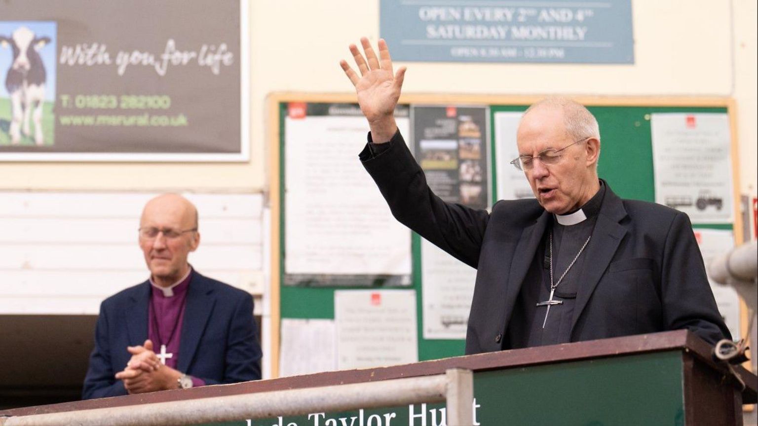 The Archbishop of Canterbury Justin Welby wearing smart clothes and a clerical collar, preying, in a hall with other people