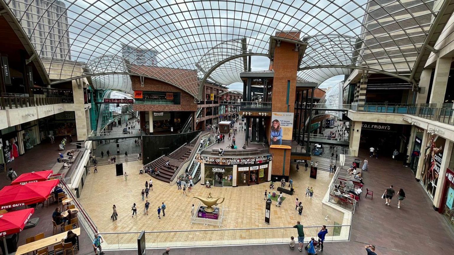 An interior image of Cabot Circus Shopping Centre in Bristol taken from the top floor showing escalators, shops and the roof