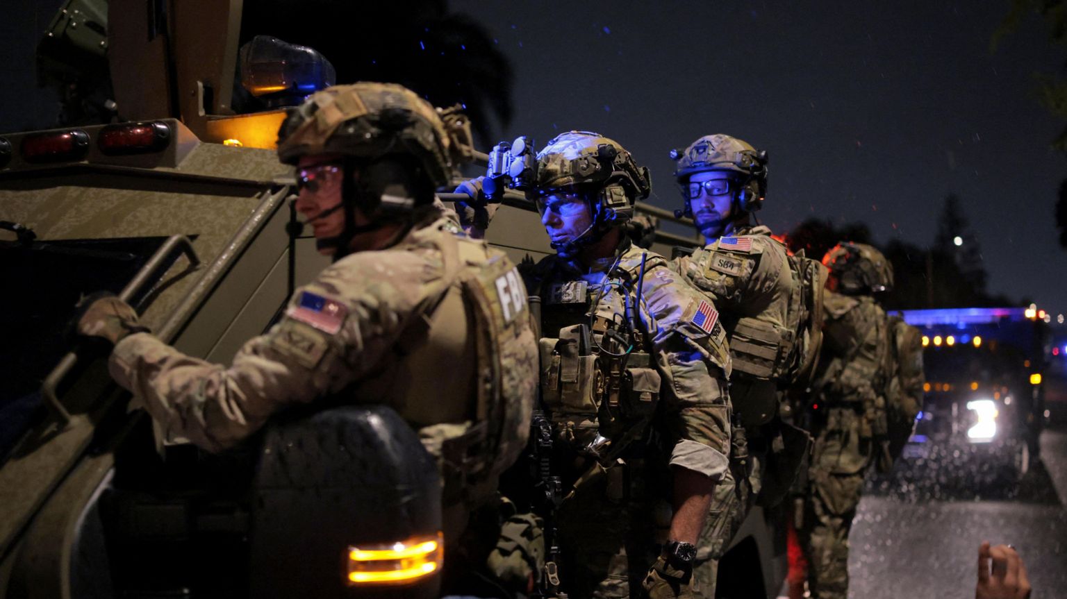 多名全副武装、戴着面罩的联邦调查局（FBI）探员，在夜间站立于一辆装甲车旁戒备